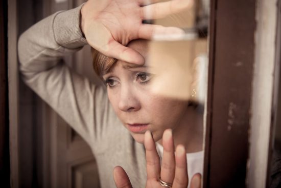Mujer mirando con preocupación a través de una ventana, reflejando tristeza y necesidad de apoyo emocional.