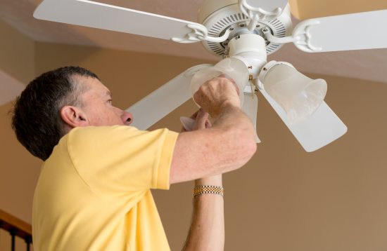 Hombre instalando un ventilador de techo moderno con aspas de madera en una habitación luminosa.