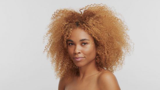 Mujer de piel morena luciendo un voluminoso afro teñido de rubio miel, mostrando un look moderno para cabello rizado.