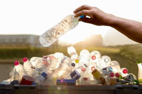 Depositando una botella de plástico en un gran contenedor de reciclaje lleno de otros envases