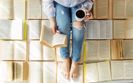 Mujer sentada entre libros, leyendo con una taza de café en la mano