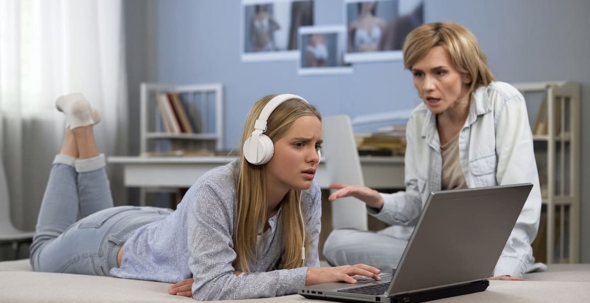 Madre y adolescente conversando mientras usan una computadora portátil, en un entorno hogareño.