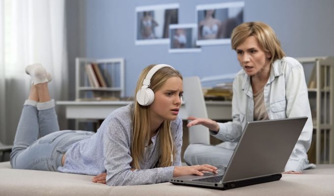 Madre y adolescente conversando mientras usan una computadora portátil, en un entorno hogareño.