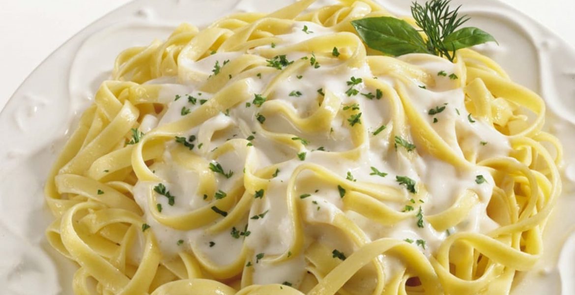 Spaguetti con salsa Alfredo en un plato blanco y decorado