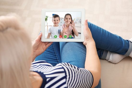 Transforma tus Momentos en Videos Inolvidables Mujer editando un video familiar en su tablet, aprendiendo a recortar y añadir música para guardar el recuerdo de una videollamada con sus hijos o nietos.