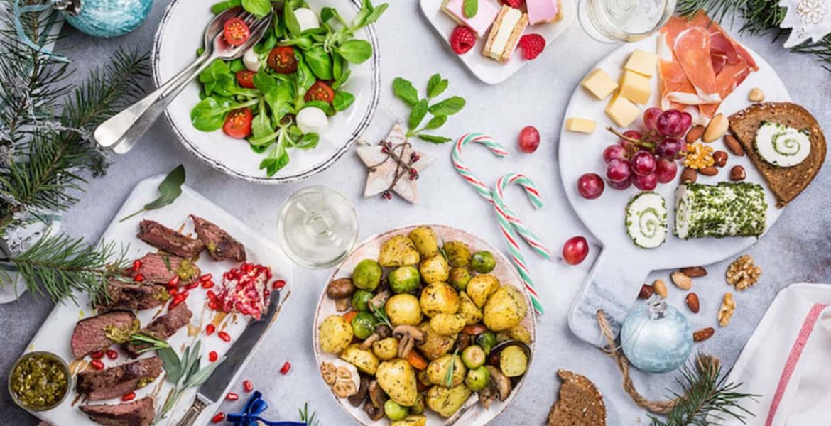 Mesa decorada con comida navideña: ensaladas, carne asada, papas al horno y postres.
