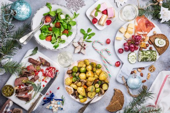 Una mesa navideña variada con carnes, guarniciones, ensaladas y dulces, ideal para compartir en familia. Mesa decorada con comida navideña: ensaladas, carne asada, papas al horno y postres.