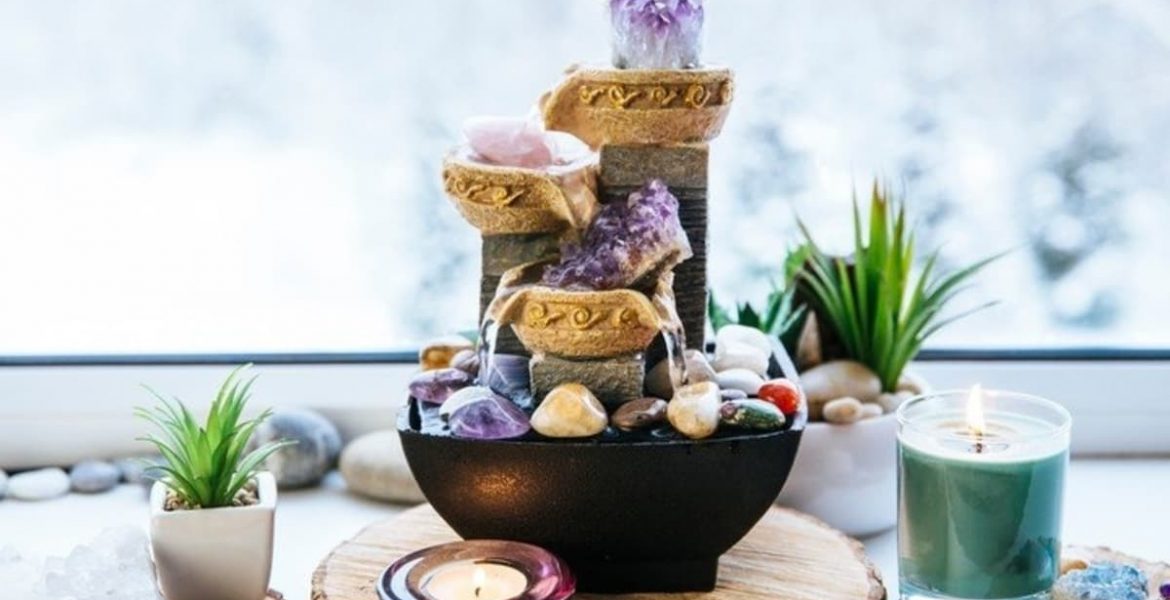 Fuente decorativa con cristales, velas y plantas sobre una mesa de madera.