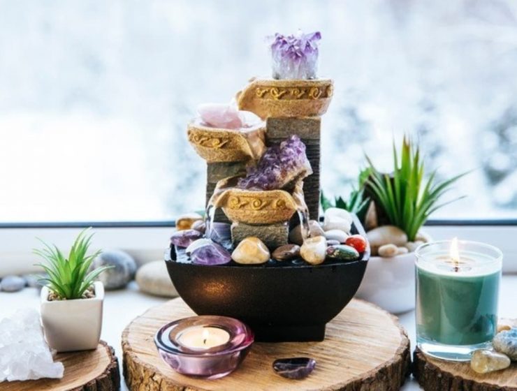 Fuente decorativa con cristales, velas y plantas sobre una mesa de madera.