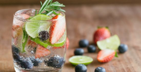 Vaso de una refrescante agua saborizada casera, infusionada con frutas frescas como fresas, arándanos y rodajas de limón.