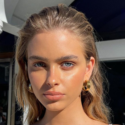 Modelo al aire libre con maquillaje natural y aretes dorados de aro