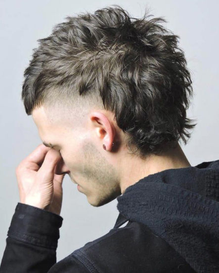 Hombre luciendo un corte de pelo mullet moderno con lados cortos desvanecidos y cabello largo y texturizado en la parte superior y en la nuca, un estilo audaz y vanguardista.
