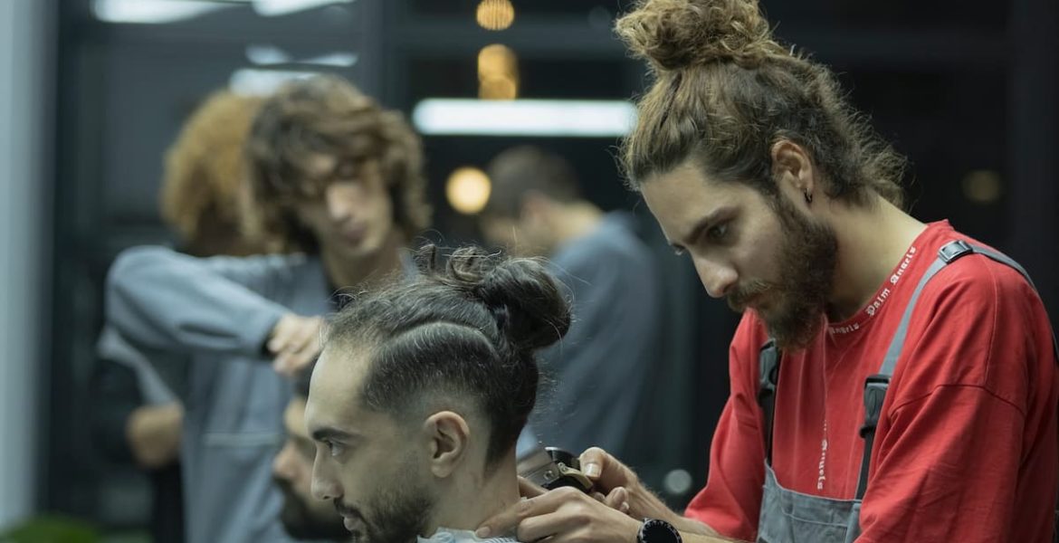 Barbero profesional concentrado, usando máquina para hacer un corte de pelo degradado o 'fade' a un cliente con un moño alto, representando la precisión en la barbería moderna.