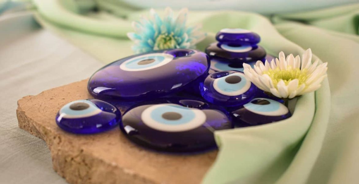 Amuletos de ojo turco azul sobre tela verde claro con flores decorativas.