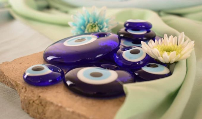 Amuletos de ojo turco azul sobre tela verde claro con flores decorativas.