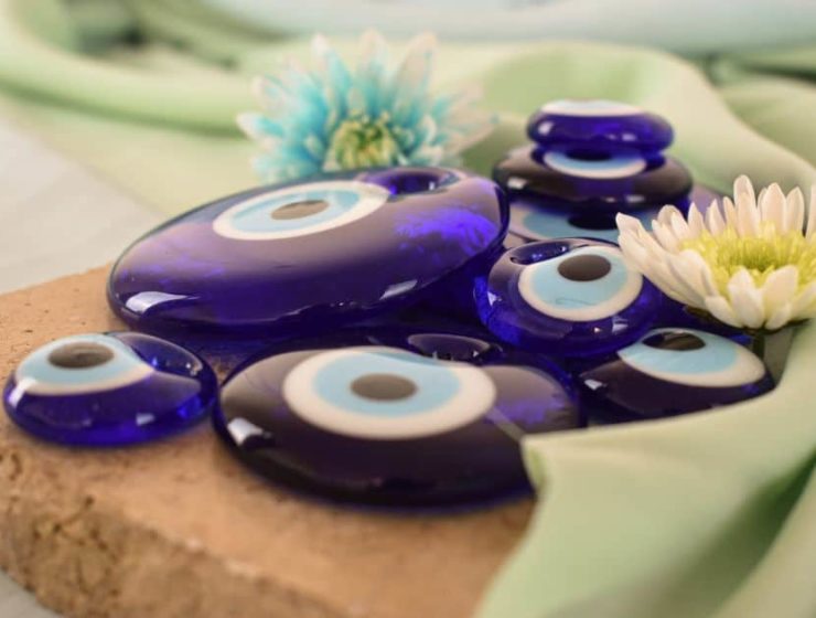 Amuletos de ojo turco azul sobre tela verde claro con flores decorativas.