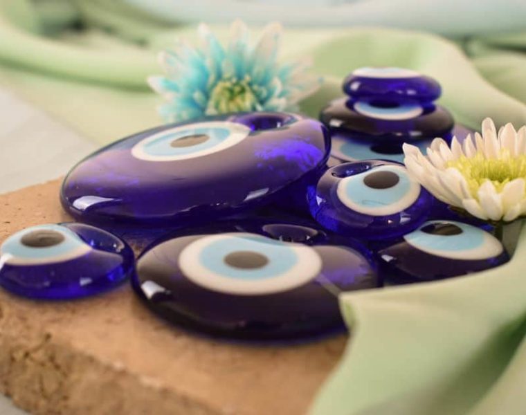 Amuletos de ojo turco azul sobre tela verde claro con flores decorativas.