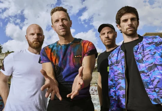 Foto promocional de Coldplay en exterior durante su tour 2025 Los cuatro miembros de Coldplay posando juntos al aire libre con cielo azul