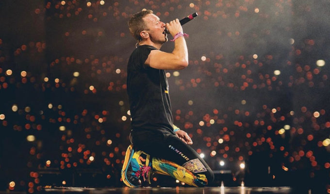 Chris Martin de Coldplay cantando con un micrófono mientras rueda en un auto en plena gira