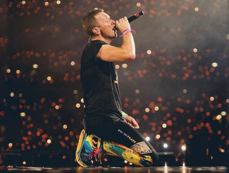 Chris Martin de Coldplay cantando con un micrófono mientras rueda en un auto en plena gira