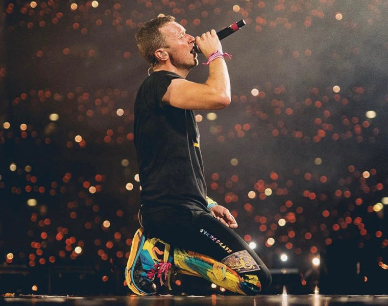 Chris Martin de Coldplay cantando con un micrófono mientras rueda en un auto en plena gira