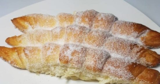 Receta Fácil de Croissants Dulces para la Familia Tres croissants dulces caseros, dorados y cubiertos de azúcar granulada, recién horneados y apilados en un plato blanco, listos para la merienda.