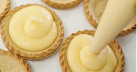 Proceso de relleno de tartaletas con crema pastelera casera de textura cremosa y brillante.