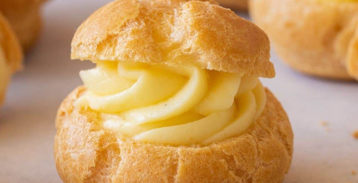 Profiterol relleno con crema pastelera, con masa dorada y textura esponjosa sobre fondo claro.