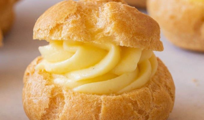 Profiterol relleno con crema pastelera, con masa dorada y textura esponjosa sobre fondo claro.