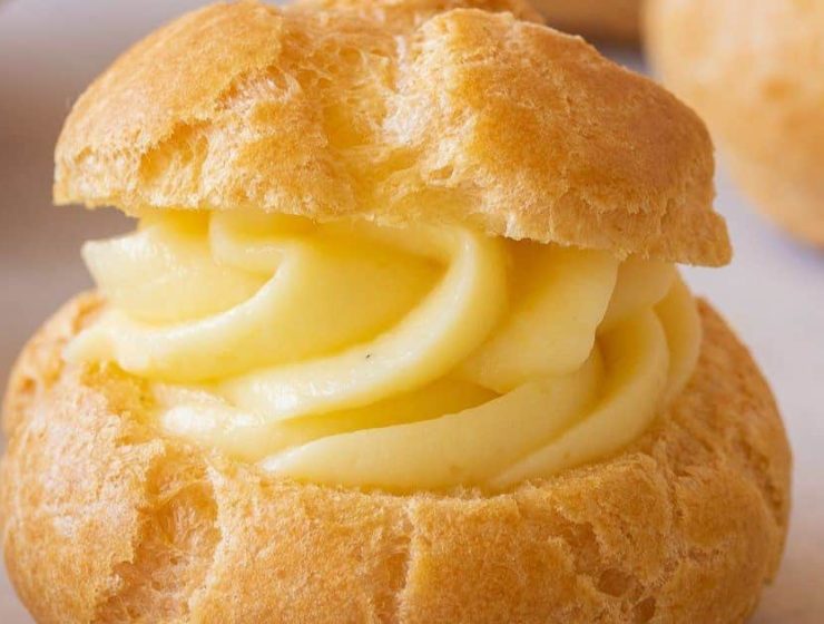 Profiterol relleno con crema pastelera, con masa dorada y textura esponjosa sobre fondo claro.