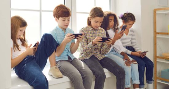 Niños sentados mirando el celular cada uno en su teléfono mostrando el uso excesivo de pantallas en la infancia