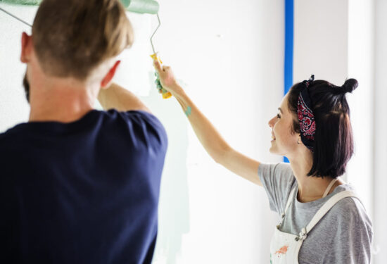 Pareja sonriendo mientras prueba una muestra de pintura en la pared para elegir el color correcto y evitar errores de decoración.