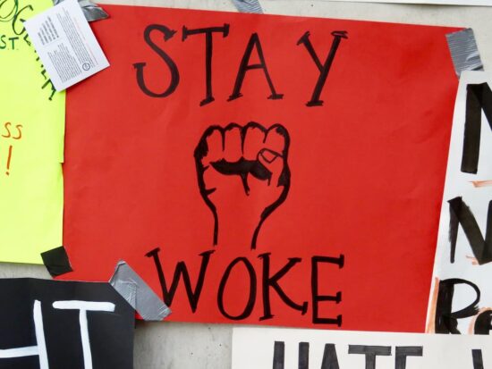 Cartel de protesta con la frase "Stay Woke" y un puño levantado, símbolo del activismo y la continua influencia del wokismo en el debate social y político