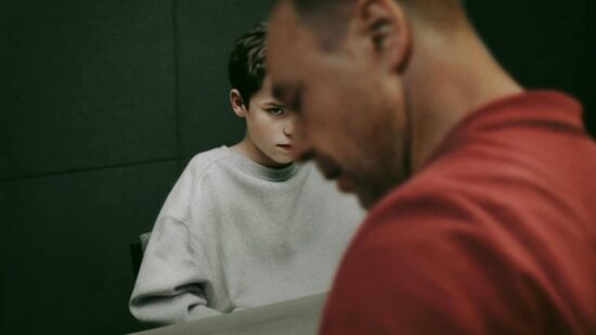 Un hijo mira con intensidad a su padre, quien está de espaldas, simbolizando el distanciamiento emocional y los errores no resueltos en la crianza.