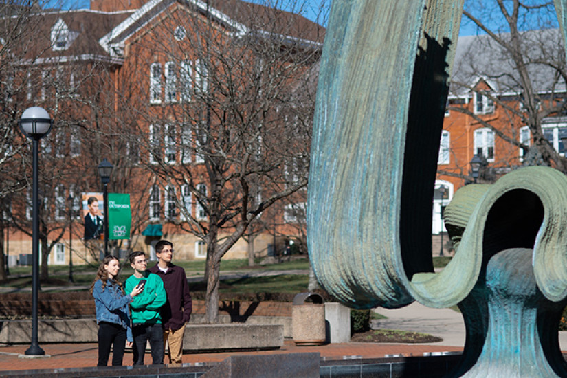 Students consult a phone and look at a public sculpture.
