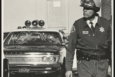A Los Angelas police officer walks away from a police cruiser with a damaged windshield.
