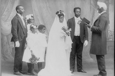 Studio photo of a preacher officiating a wedding, as the best man, flower girls, and ring bearer watch, 1908.