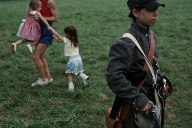 Image of a young boy carrying a pistol with women and children in the background.