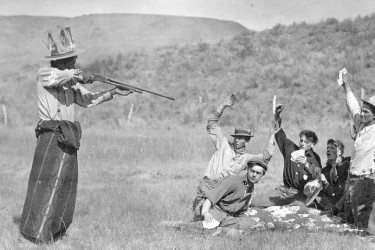 Frank Matsura photograph: a staged scene of a Native American man using a rifle to hold up men playing cards.