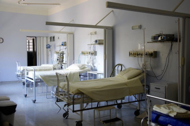 A row of three empty hospital beds in a white room.