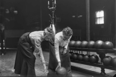 A woman showing another woman how to throw a bowling ball.