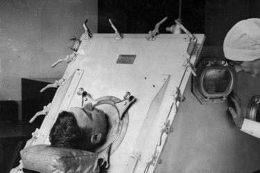 Nurse attends man in iron lung.
