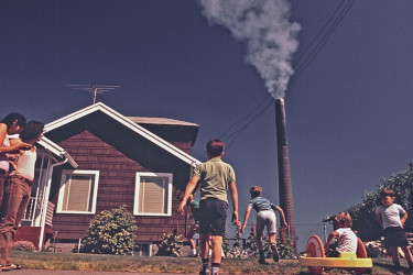 Children standing in front of a house and pollution/smoke in background.