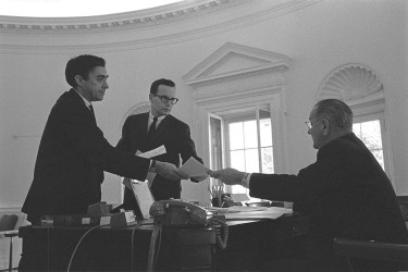 Staff handing Lyndon Johnson reports in the oval office.