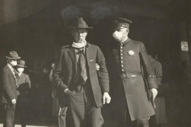 Police officer wearing a mask, arrests a man who lowered his mask to smoke a pipe, in 1918.