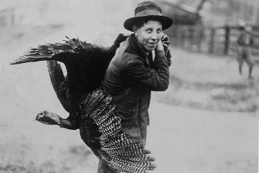 Boy carrying a live turkey over his shoulder.