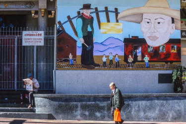 Two Chinese-American men by a mural celebrating the transcontinental railroad in San Francisco's Chinatown.