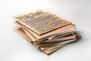 "We The People" Constitution on top of many folders of paper.