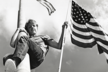 Teenager holding a U.S. flag while scaling a flagpole.