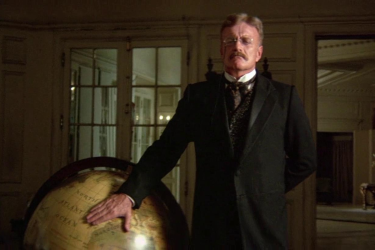 Brian Keith as Theodore Roosevelt putting his hand on a globe in a 1975 film.